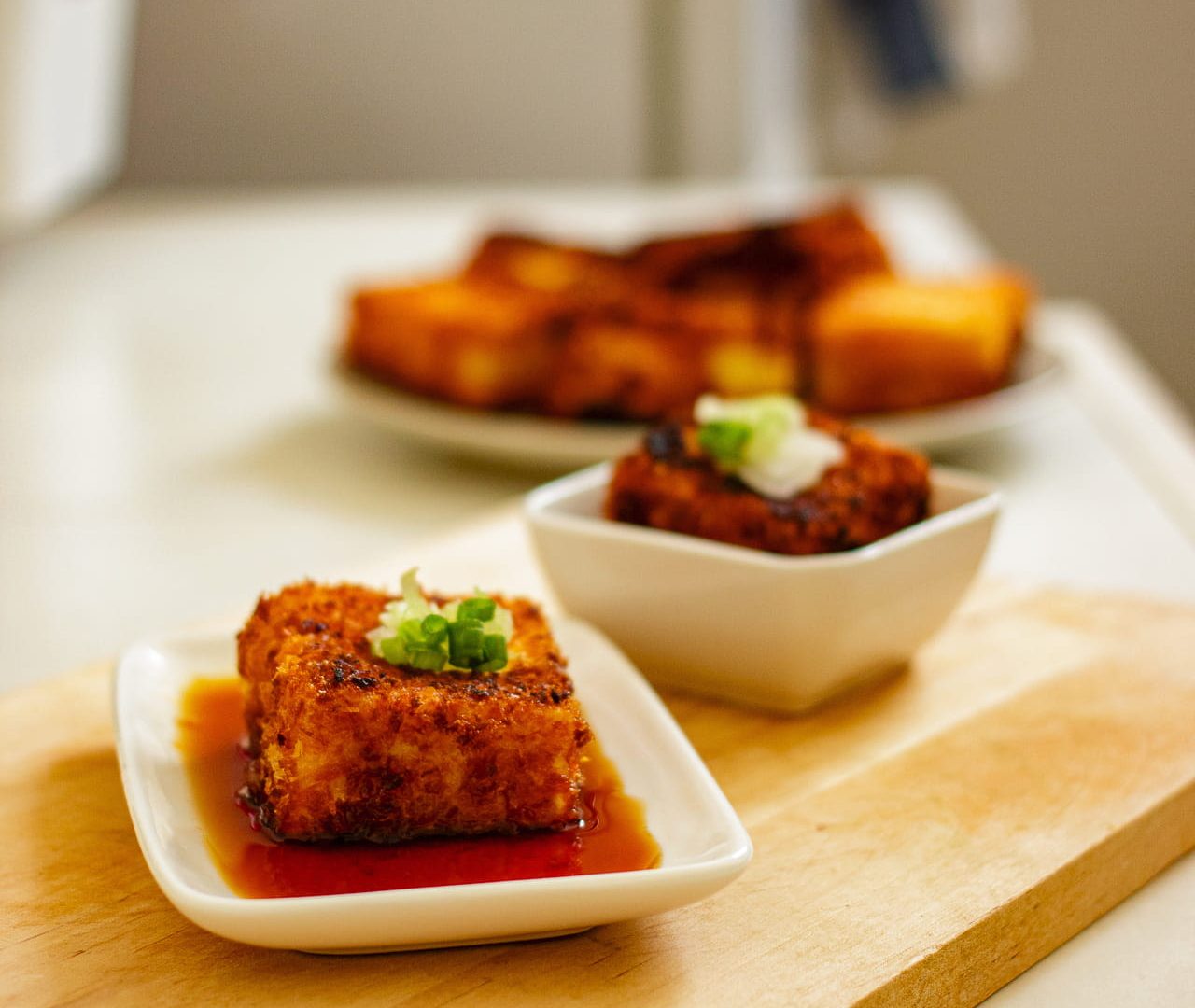 Crispy fried tofu with ponzu sauce and spring onion on a cutting board