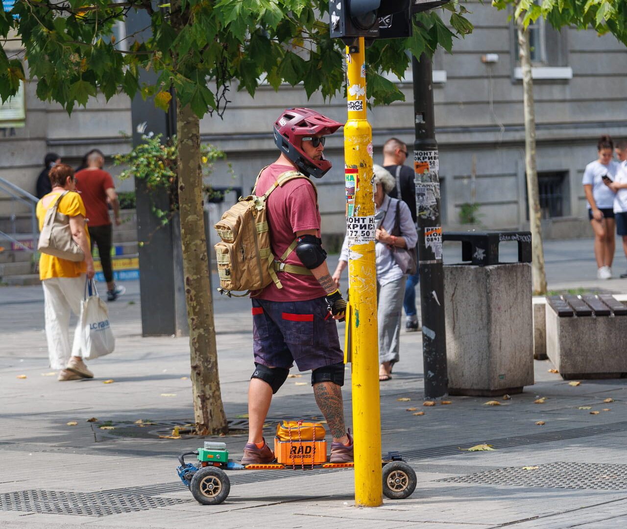 Street performer in cycling gear standing beside yellow traffic light pole with custom RAD cart at pedestrian crossing in Sofia, Bulgaria