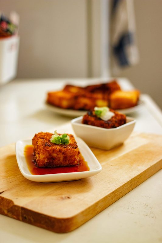 Crispy fried tofu with ponzu sauce and spring onion on a cutting board