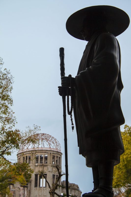 Silhouette of a Buddhist monk statue with prayer beads against the Atomic Bomb Dome in Hiroshima