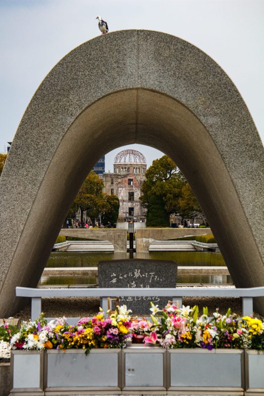 Hiroshima Peace Memorial cenotaph framing the Atomic Bomb Dome with flower offerings