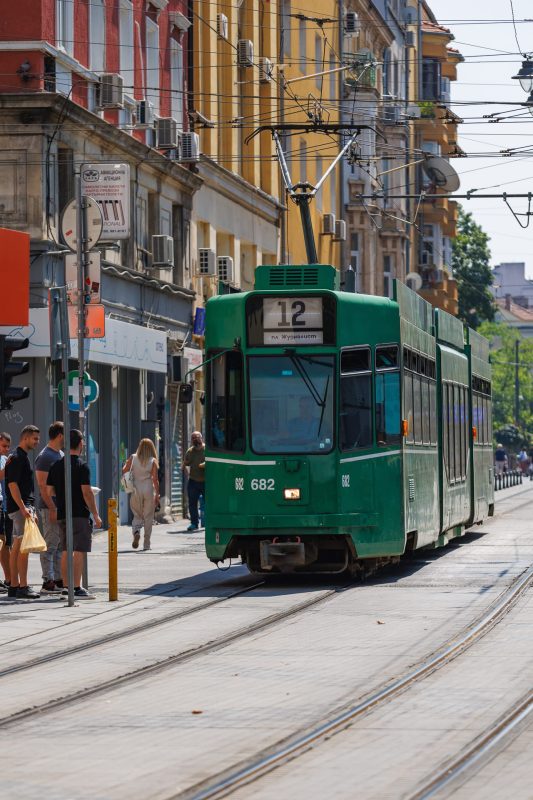 Green vintage tram number 682 on line 12 approaching through residential street with colorful buildings and overhead wires in Sofia, Bulgaria